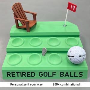 May include: A green tiered golf ball display stand with the text "RETIRED GOLF BALLS". It features a miniature wooden chair, a golf ball, a golf tee, and a red flag with the number 19. The stand has multiple circular indentations for golf balls.