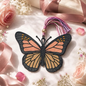 May include: Embroidered butterfly with orange and yellow wings, outlined in black. The butterfly has a tassel with pink, purple, and white threads, and a gold bead. The background includes pink roses and ribbons.