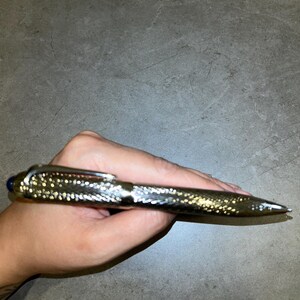 Peut inclure: Un stylo à bille argenté doté d'un corps métallique texturé à motifs croisés et d'un clip poli. Le stylo présente une extrémité de capuchon arrondie avec un petit accent circulaire bleu foncé au sommet, et une pointe métallique lisse et effilée.