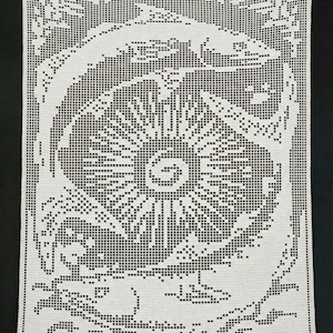 May include: White crocheted textile with a detailed, symmetrical design. The central motif is a stylized sunburst, surrounded by floral and scrollwork patterns. The piece is displayed against a black background, highlighting the intricate openwork.