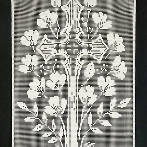 Puede incluir: Un tapiz de pared blanco tejido a ganchillo con un diseño de árbol. El intrincado patrón presenta un tronco central con ramas, flores y hojas. El fondo es negro liso, resaltando el detallado trabajo de ganchillo blanco. La pieza es rectangular.