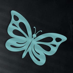 May include: A large, turquoise butterfly wall decoration is mounted on a dark wall. The butterfly has intricate cut-out details in its wings. The background includes a dark sofa with teal pillows and a shelf with vases.