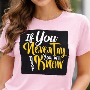 May include: A light pink t-shirt with the text "If You Never Try You Will Never Know" in white and yellow lettering on a black rectangle. The shirt has short sleeves and a crew neck.