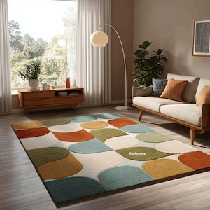 May include: A colorful area rug with an abstract design of overlapping shapes in shades of orange, green, blue, and yellow. The rug is placed in a living room setting with a sofa, wooden furniture, and a floor lamp.