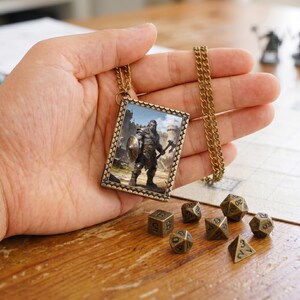 Puede incluir: Un collar con colgante rectangular que presenta un marco de metal en tono bronce y una cadena. El colgante muestra una ilustración impresa de un guerrero orco sosteniendo un escudo y un hacha frente a un castillo de piedra. Siete dados poliedros.