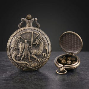 May include: Bronze pocket watch with a detailed relief of a knight fighting a dragon. The watch face features a sword and shield design. Beside it, an open matching case holds several dice, suggesting a role-playing game theme.
