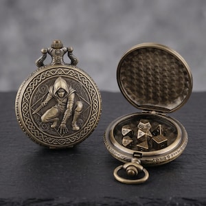 Può includere: Orologio da tasca antico in bronzo con un rilievo dettagliato di una figura incappucciata. L'orologio è aperto, rivelando un set di dadi poliedrici. L'orologio ha un anello decorativo e un retro strutturato.