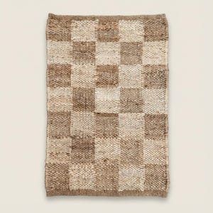 May include: A rectangular, woven rug with a checkerboard pattern. The squares alternate between light beige and various shades of brown. The rug has a textured surface and a natural, earthy aesthetic.