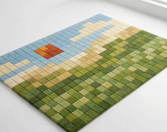 May include: A rectangular area rug with a pixelated landscape design. The rug features a blue sky with a red and orange sun, transitioning into a beige and green field. The rug is made of a soft, textured material.
