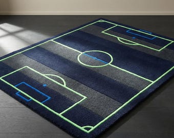 May include: A rectangular rug designed to resemble a soccer field. The rug features a navy blue background with gray stripes and green outlines. The goal boxes and center circle are clearly defined, creating a playful, sporty aesthetic.