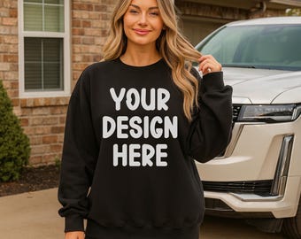 May include: A black sweatshirt with the text "YOUR DESIGN HERE" in white block letters. The sweatshirt is worn by a person standing in front of a house and a white SUV. The person is also wearing black shorts.