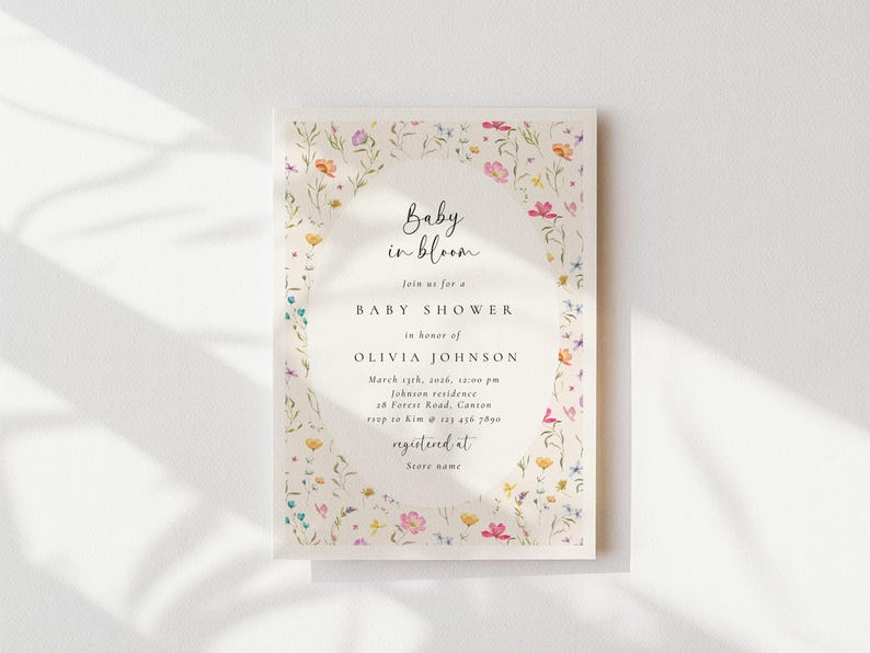 Może przedstawiać: Zaproszenie na baby shower z kwiatową obw&oacute;dką. Zaproszenie zawiera tekst "Baby in bloom" i szczeg&oacute;ły wydarzenia w eleganckiej czcionce. Projekt obejmuje kolorowe dzikie kwiaty i zieleń, tworząc delikatną estetykę.