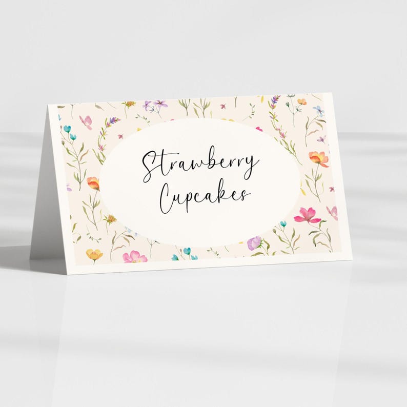 May include: A folded card with a floral design and the words "Strawberry Cupcakes" in elegant script. The card features a cream background with colorful flowers and greenery, perfect for a dessert table.