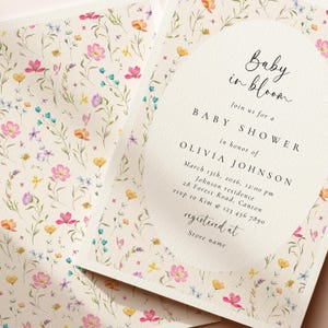 May include: Baby shower invitation with a floral design. The invitation features the text "Baby in bloom" and details for Olivia Johnson's baby shower, including the date, time, and location. The invitation is decorated with colorful watercolor flowers.
