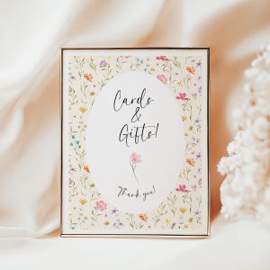 May include: A framed sign with a floral design and the words "Cards & Gifts!" in elegant script. The sign features a cream background with colorful flowers and greenery, and a gold frame. The words "Thank you!" are at the bottom.