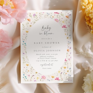 May include: A baby shower invitation with a floral design. The invitation features the text "Baby in bloom" and details for Olivia Johnson's baby shower, including the date, time, and location. The invitation is decorated with colorful flowers.