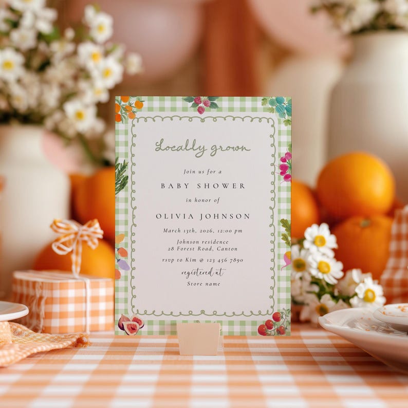 May include: A baby shower invitation with a green gingham border and floral illustrations. The text reads "Locally grown" and details for Olivia Johnson's baby shower, including the date, time, and location. The invitation is propped up on a table.