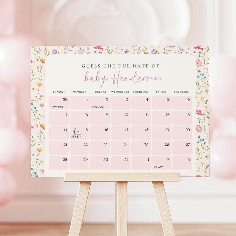 May include: A pink and floral baby shower calendar on a wooden easel. The calendar reads "Guess the Due Date of baby Henderson" and includes dates from November to January. The calendar is decorated with floral accents.