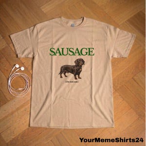 May include: Tan t-shirt with the word "SAUSAGE" in green above a brown dachshund illustration. Below the dog is the text "(Do not eat)". The bottom right corner of the shirt has the text "YourMemeShirts24".