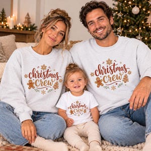 May include: Two adults and one child wearing light gray crewneck sweatshirts and a white t-shirt, all featuring the text "christmas crew" in brown script, surrounded by gingerbread man, tree, and snowflake illustrations.