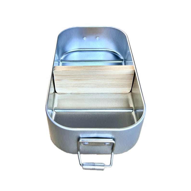 May include: A rectangular silver-colored metal lunch box with rounded corners and a metallic finish. The interior features a removable light-colored wooden divider placed across the center. A small metal handle is attached to the front exterior.
