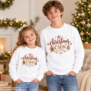 May include: Two white long-sleeve sweatshirts featuring a graphic print that says "christmas crew" in brown script, surrounded by illustrations of a gingerbread person, a Christmas tree, and snowflakes in brown, red, and green colors.