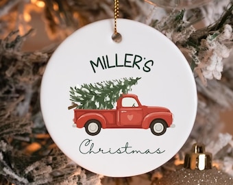 May include: A round white ceramic ornament featuring a red vintage pickup truck carrying a green Christmas tree. The text MILLER'S is printed in dark green above the truck, and the word Christmas is printed in black script below the truck.