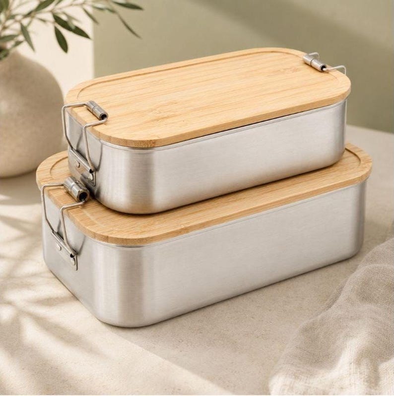 May include: Two rectangular food containers stacked on top of each other. Each container features a brushed silver metal base with rounded corners and a light-colored bamboo wood lid. Metal wire latches secure the lids to the containers.