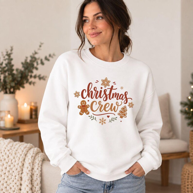 May include: A white long-sleeve crewneck sweatshirt featuring a graphic print with the text "christmas Crew" in brown script, surrounded by illustrations of a gingerbread man, a Christmas tree, stars, and snowflakes.