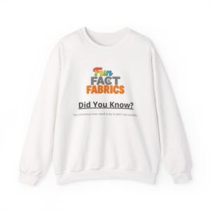 Op de afbeelding: Witte crewneck sweatshirt met de tekst "Fun Fact Fabrics" in een kleurrijk ontwerp. Onder het logo staat de tekst "Did You Know?", gevolgd door een feit over kerstbomen.