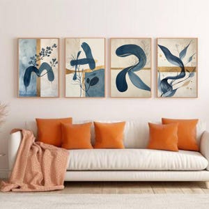 May include: Four framed abstract art prints with blue and gold accents hang above a white sofa with orange throw pillows and a peach-colored blanket. The artwork features flowing shapes and botanical elements.
