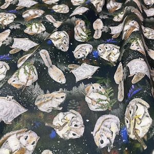 May include: A dark fabric featuring a repeating pattern of white and light brown flying squirrels. The squirrels are depicted in various poses, some holding small green pine branches, set against a black background with white speckles.