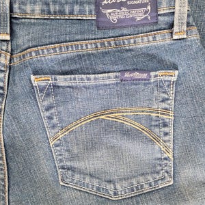 May include: Close-up of blue denim jeans featuring a back pocket with a curved stitch design. The Levi Strauss Signature label is visible on the pocket and waistband. The jeans have a classic, worn look.