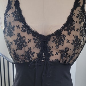 May include: Black slip dress with a sheer, floral lace bodice. The lace detailing is black and covers a nude-colored fabric. The dress has a low neckline with a lace-up detail and a fitted silhouette.