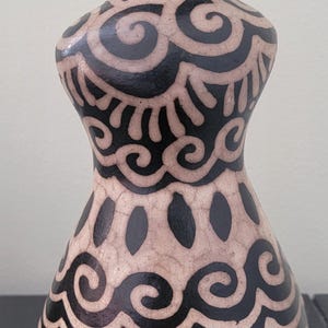 May include: A decorative ceramic vase with a beige base and black, swirling patterns. The vase has a flared base and a narrow neck. The design includes stylized sunbursts and oval shapes. The vase is approximately 8 inches tall.
