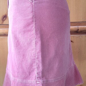 Op de afbeelding: Een roze corduroy rok met een uitlopende zoom. De rok heeft een klassiek ontwerp met vijf zakken, waaronder een voorzak. De stof heeft een verticale ribtextuur. De rok is effen roze van kleur.