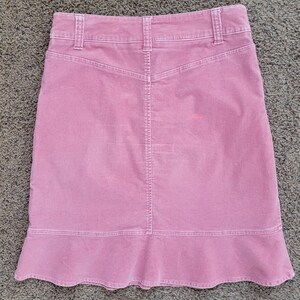 Op de afbeelding: Een stoffen roze corduroy rok met een uitlopende zoom. De rok heeft een klassiek ontwerp met vijf zakken, een tailleband en riemlussen. De achterkant heeft een rugstuk en een verticale naad in het midden.