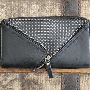 May include: Black wallet with a silver zipper and a dotted pattern. The wallet has a diagonal zipper design and a black leather pull tab. The wallet is rectangular and appears to be made of leather.