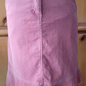 Op de afbeelding: Een stoffen rok in stoffig roze met een knoopsluiting en een gefranjerde zoom. De rok heeft een klassiek ontwerp met vijf zakken en een getailleerd silhouet. De rok is gemaakt van een zachte, getextureerde corduroy stof.