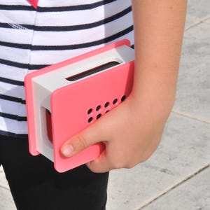May include: A pink and white rectangular object with a handle is held in a person's hand. The object has a series of small, evenly spaced holes on one side. The person is wearing a striped shirt.