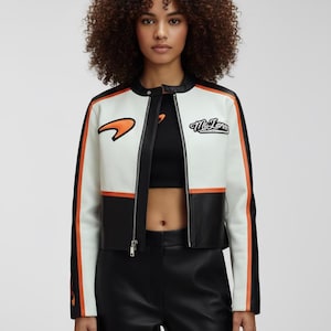 May include: White, black, and orange racing jacket with a zip-up front. The jacket has black sleeves with orange stripes and the McLaren logo on the chest. The jacket is cropped and made of leather.