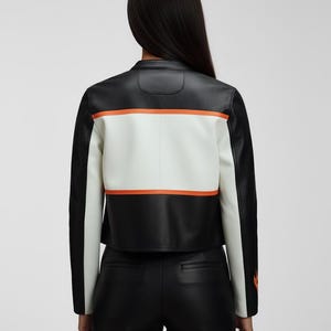 May include: Black and white leather jacket with orange stripe accents. The jacket features a white panel across the back with an orange stripe above and below. The sleeves and shoulders are black. The jacket is cropped.