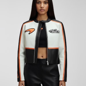 May include: A cropped, white, black, and orange leather jacket with a round collar and a zipper closure. The jacket features a McLaren logo and lettering on the chest. The sleeves have orange stripes.