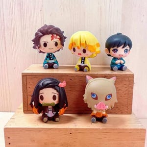 May include: Five chibi-style figurines of anime characters. The figures are on a wooden display. The characters have distinctive hair colors and outfits, including yellow, black, and brown. Each figure is approximately 2 inches tall.
