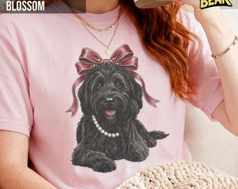 May include: Pink t-shirt with a graphic of a black dog wearing a bow and pearl necklace. The dog has a happy expression. The text "COMFORT COLORS BLOSSOM" is at the top left, and the text "LUNATIC BEAR" is at the top right.