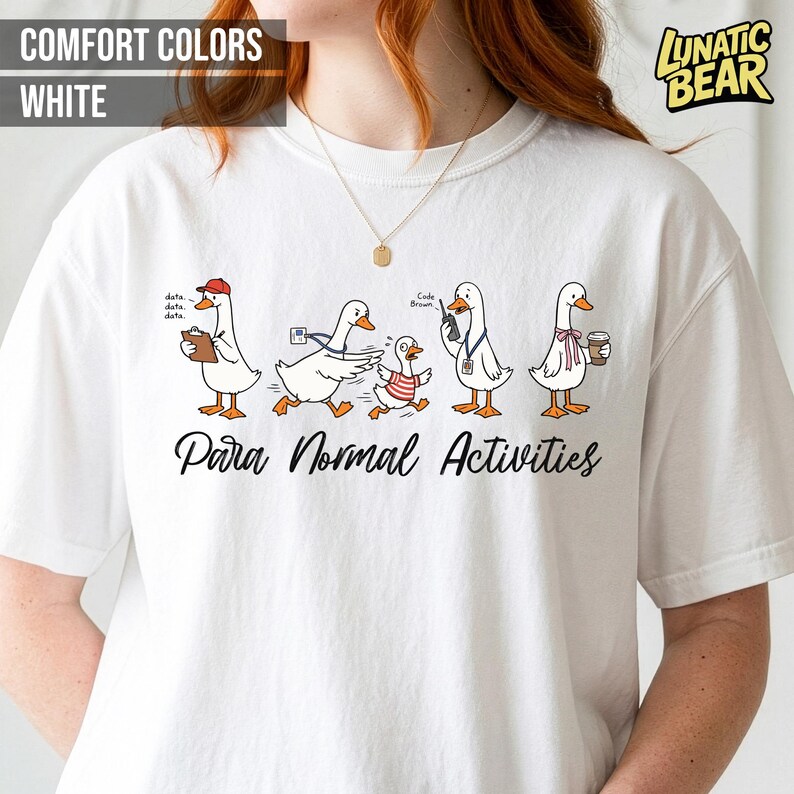 May include: White t-shirt with a graphic of cartoon geese engaged in various activities. The geese are depicted with accessories like a clipboard, a messenger bag, and a coffee cup. The text "Para Normal Activities" is printed below the geese.