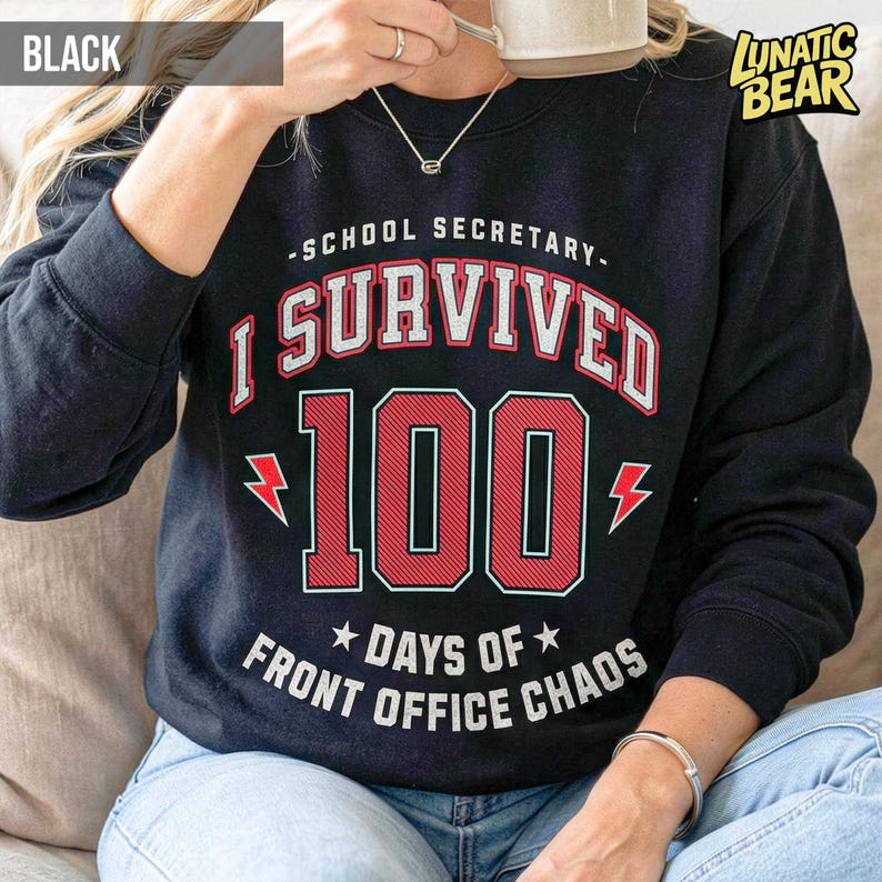 May include: Black sweatshirt with the text "-SCHOOL SECRETARY- I SURVIVED 100 DAYS OF FRONT OFFICE CHAOS." The text is in white and red. The number 100 is in a bold, red font. The sweatshirt has long sleeves.