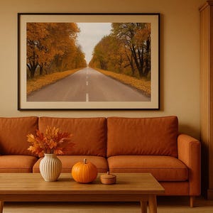 Könnte beinhalten: Ein gerahmter Landschaftsdruck zeigt eine Straße mit Bäumen in Herbstfarben. Vor dem Druck befinden sich ein orangefarbenes Sofa, ein Holztisch und ein Kürbis. Eine Vase mit Herbstblättern und ein Holzschrank vervollständigen die Szene.