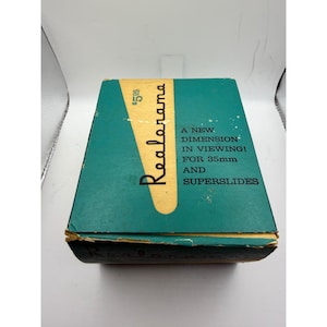 May include: Vintage teal Realorama box with the text "A New Dimension in Viewing! For 35mm and Superslides." The box has a yellow vertical stripe with the word "Realorama" in black script. The price tag shows $5.95.