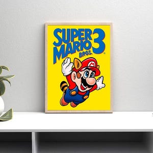 Könnte beinhalten: Gerahmtes Poster mit Super Mario Bros. 3. Das Kunstwerk zeigt Mario in seinem Waschbär-Anzug vor einem leuchtend gelben Hintergrund. Der Titel ist blau, mit der Zahl 3 oben rechts. Das Poster ist in einem Holzrahmen.